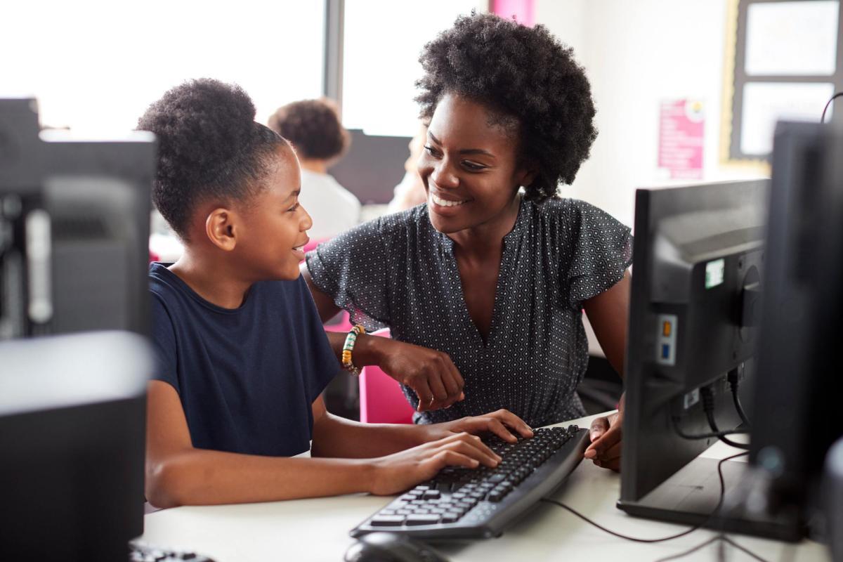 A Black educator works one-on-one in a school computer lab