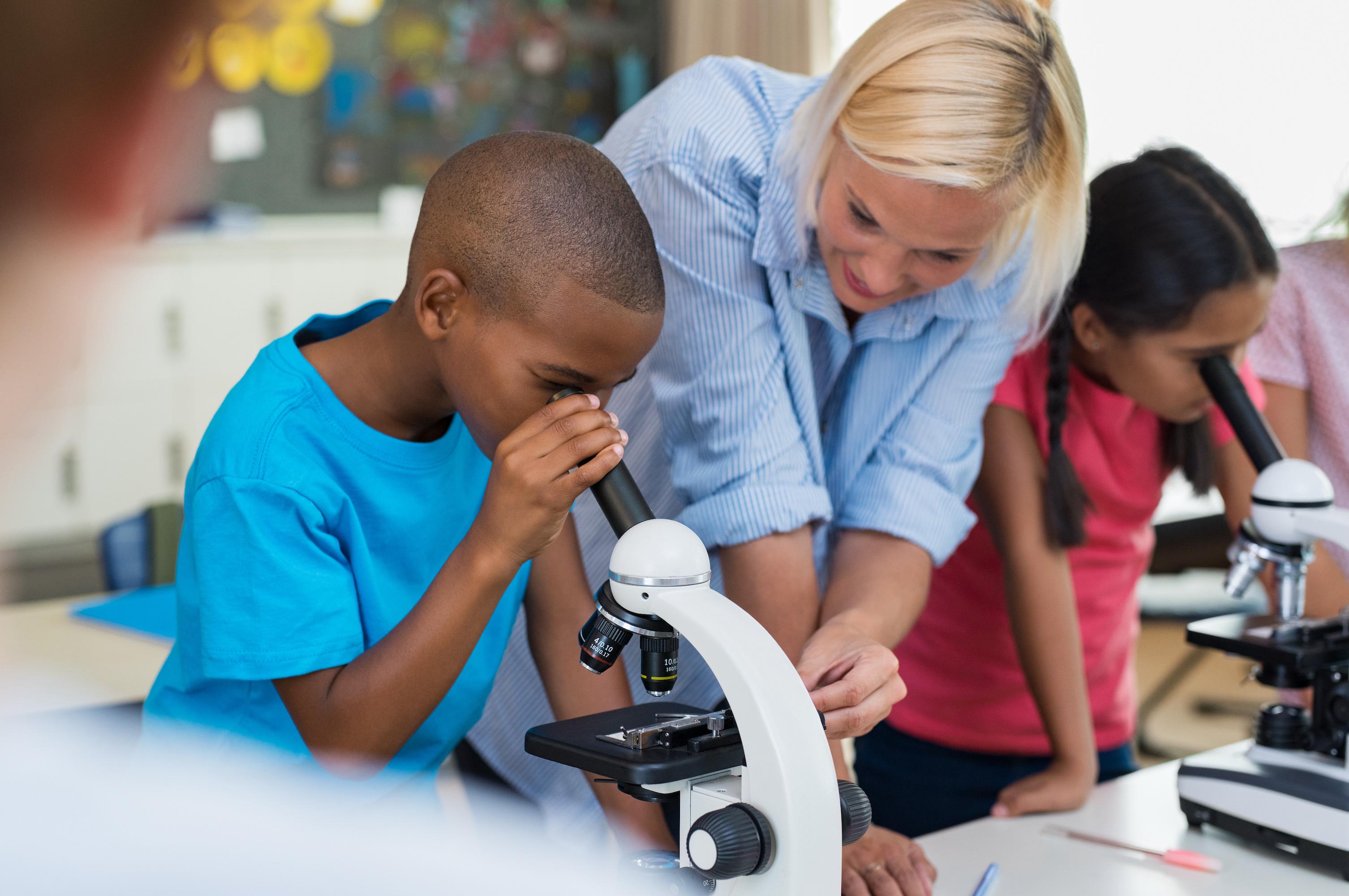 Female teacher guiding students using microscope.