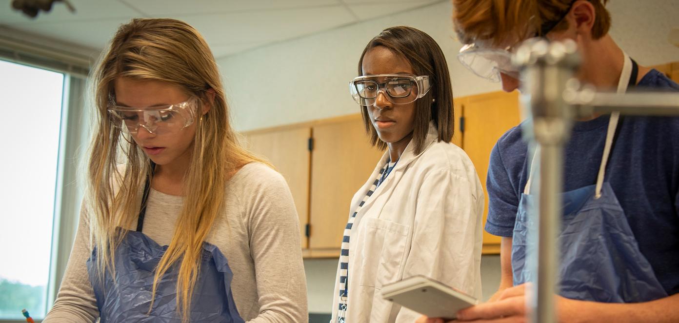 Three students in school laboratory wearing lab safety glasses.