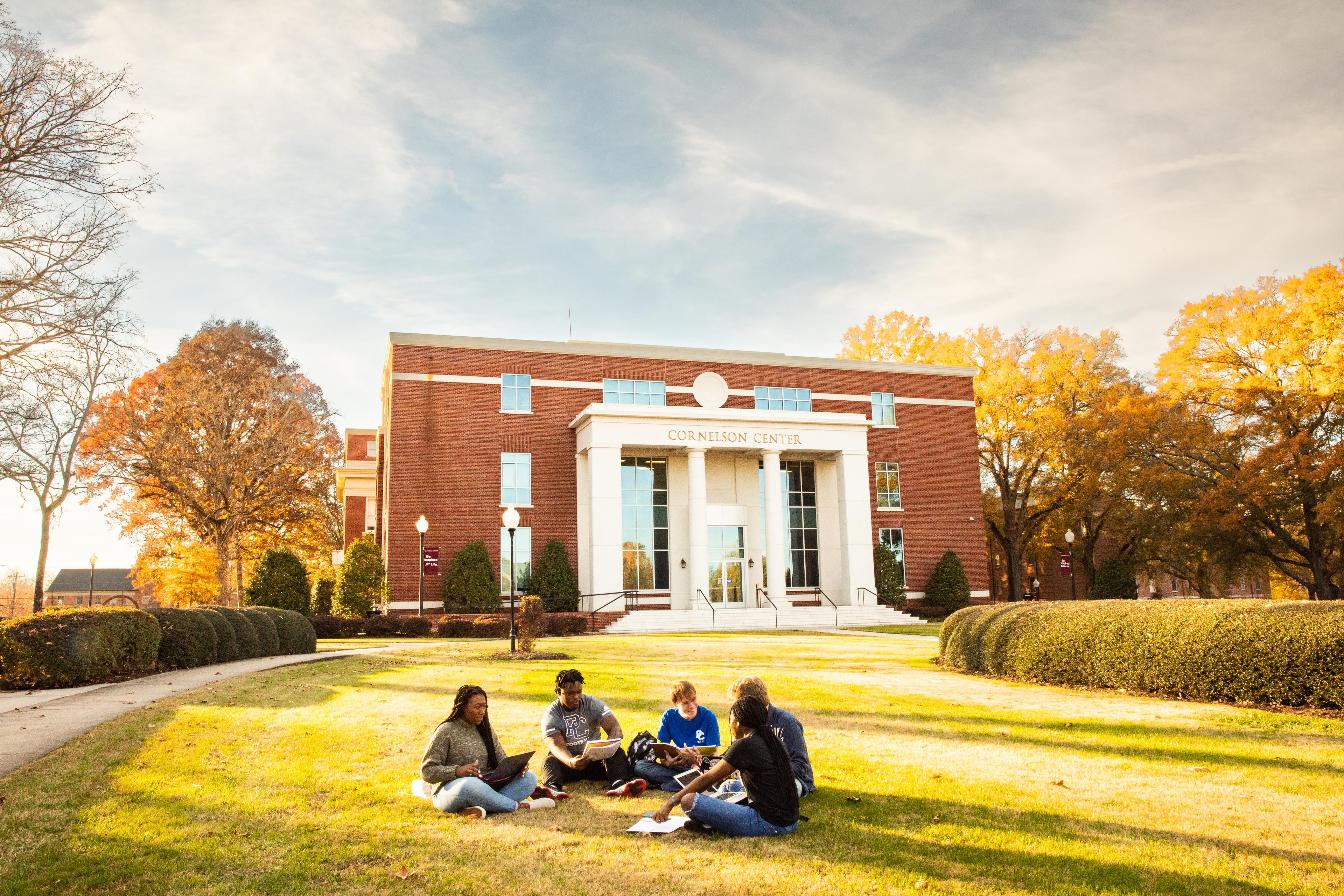 Five college students seated on the school grounds in front of Presbyterian College's Cornelson Center building; appear to be discussing.
